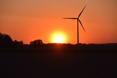 Silhouette wind turbines on field against romantic sky at sunset