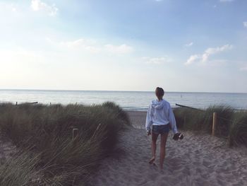 Rear view of woman walking at beach against sky