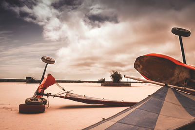 Fallen land sailboards on field against cloudy sky