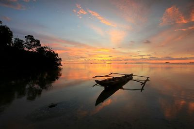 Silhouette boat moored in sea against sky during sunset