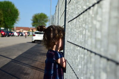 Girl looking through fence in city