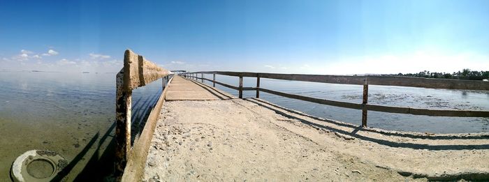 Jetty leading to calm sea against blue sky