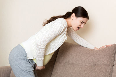 Side view of young woman against wall at home