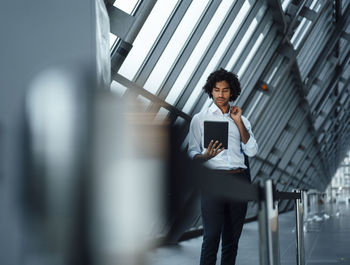 Confident businessman using digital tablet while standing by barricade at office