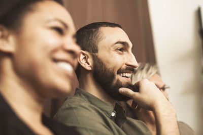 Happy businessman looking away while sitting with female colleagues in office