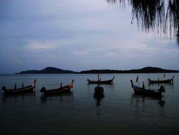 Boats in sea against cloudy sky