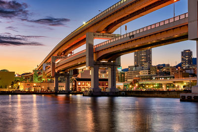 Illuminated bridge over river against sky at dusk