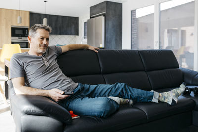 Mature man holding remote control while sitting on sofa at home