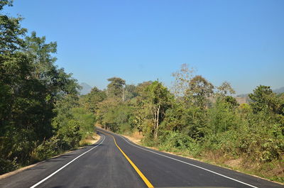 Empty road along trees and plants against sky