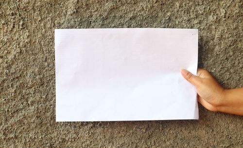 Low section of person holding paper against wall