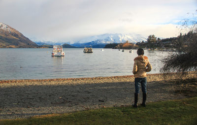 Rear view of man standing on riverbank against sky