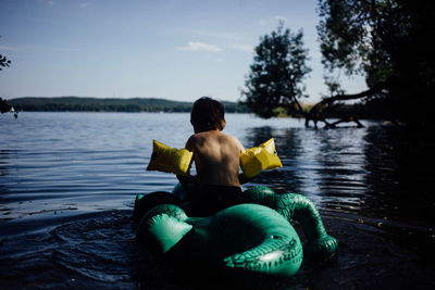 Rear view of boy sitting on lake against sky