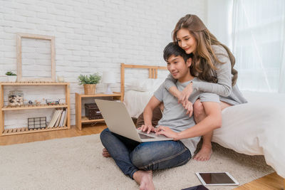 Smiling young woman using phone while sitting on floor