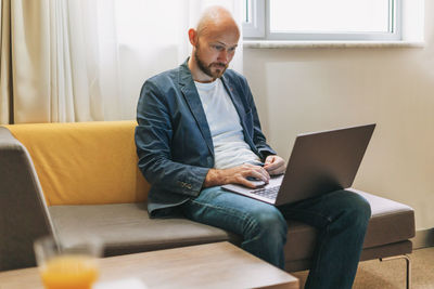 Smiling businessman using laptop sitting on sofa at home