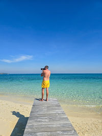 Rear view of woman standing at beach against clear blue sky