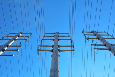 Low angle view of electricity pylon against clear blue sky