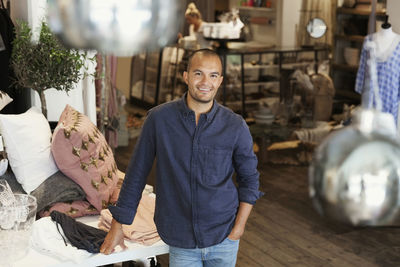 Portriat of smiling male owner standing by clothes on table at store