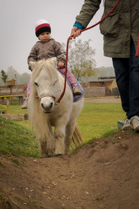 Girl riding pony while mother holding rope on field