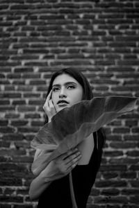 Side view of young woman holding leaf against brick wall