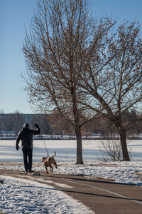 Rear view of man with dog on road amidst snow covered field