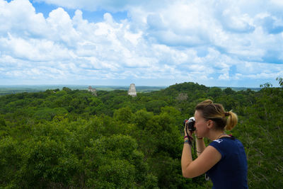 Woman photographing trees against sky