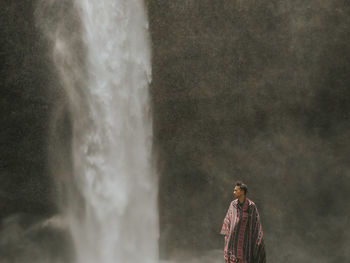 Man standing against waterfall falling from mountain