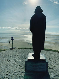 Rear view of man standing on beach against sky