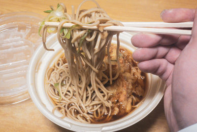 Close-up of hand holding bowl of noodles