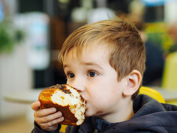 Cute toddler boy in casual clothes eating a chocolate bun in a food court