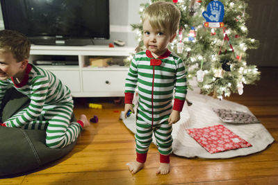 Toddler boy standing in front of christmas tree in green striped pjs