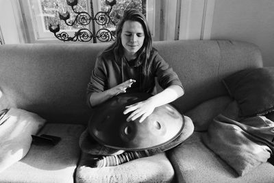 High angle view of young woman playing handpan while sitting on sofa at home