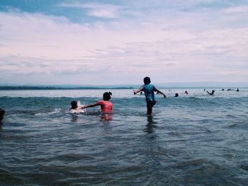 People enjoying on sea against cloudy sky