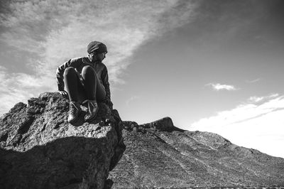 Low angle view of woman sitting on rock against sky