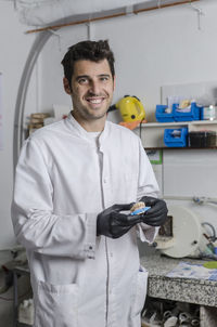 Portrait of smiling dentist holding dentures in laboratory