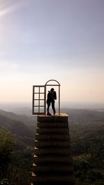 Couple kissing while standing on staircase against sky during sunset