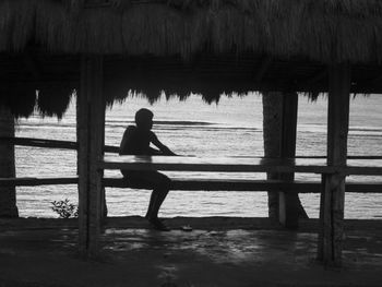 Silhouette of man sitting on wood at beach