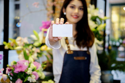 Portrait of female florist showing blank business card in flower shop