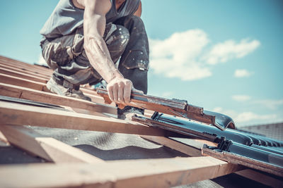 Man working on wood against sky