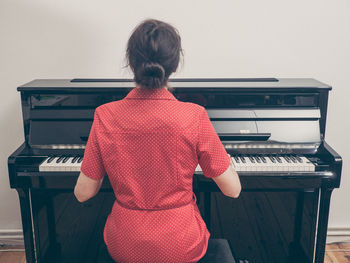 Rear view of woman playing piano at home