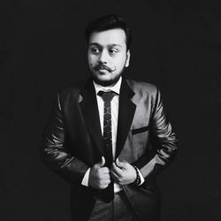 Young man wearing suit while standing against black background