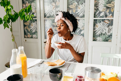 Young black woman with closed eyes enjoying tasty dish while sitting at table and having breakfast in morning at home