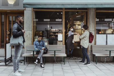 Customers maintaining social distancing while collecting order at deli store during pandemic