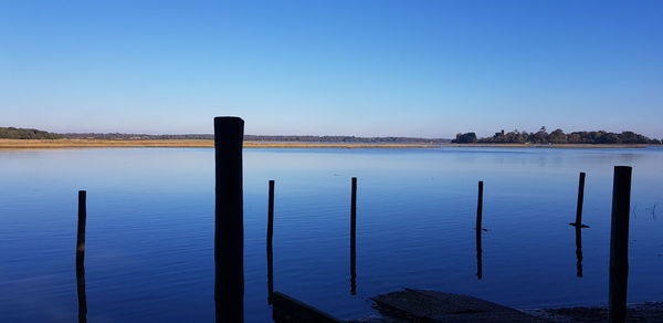 Wooden posts in lake against clear blue sky