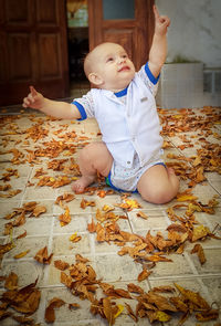 Cute boy sitting on leaves at home