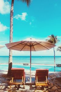 Chairs by swimming pool at beach against blue sky