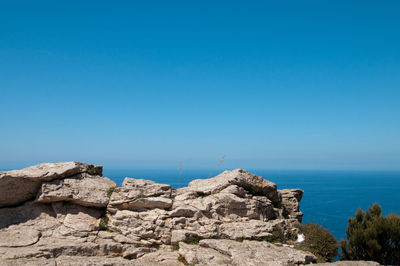 Rocks by sea against clear blue sky