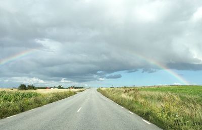 Road passing through landscape against storm clouds