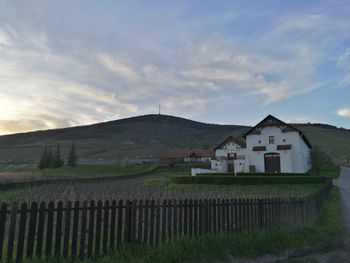 House on field by houses against sky