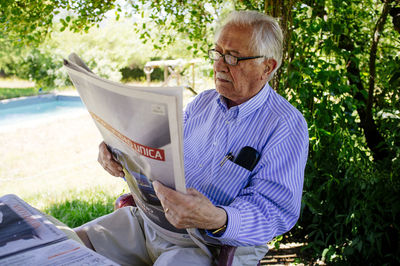 Senior man reading newspaper while sitting against tree