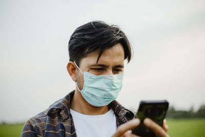 Man using mobile phone while wearing mask against sky